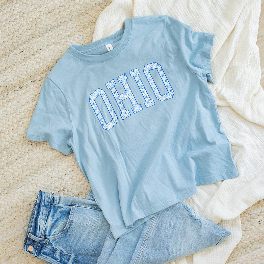 Light blue t-shirt with 'OHIO' text and denim shorts on a beige surface