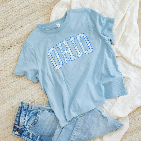 Light blue t-shirt with 'OHIO' text and denim shorts on a beige surface