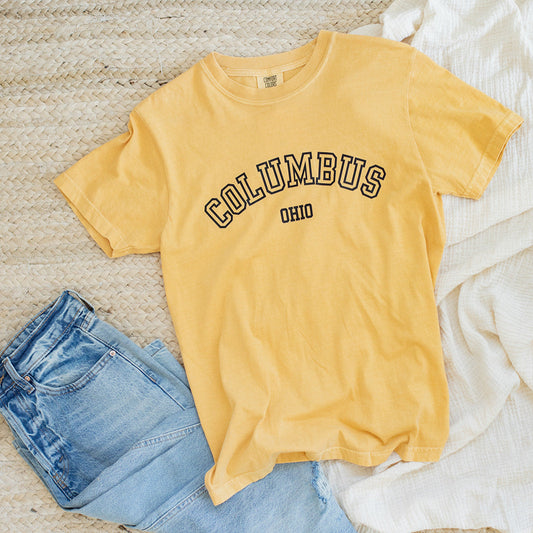 Yellow t-shirt with 'Columbus, Ohio' text on a textured surface with jeans and a white cloth.