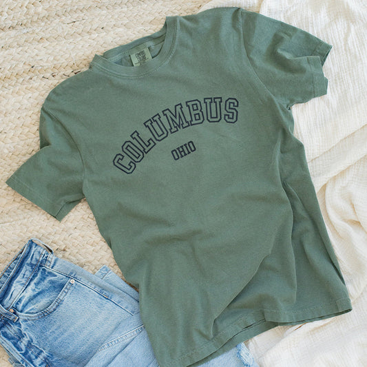 Green t-shirt with 'Columbus' text and blue jeans on a textured surface