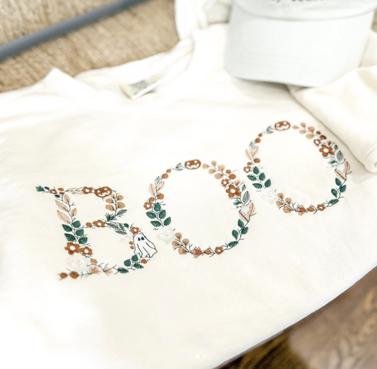 A white t-shirt with the word "BOO" embroidered in a floral design.